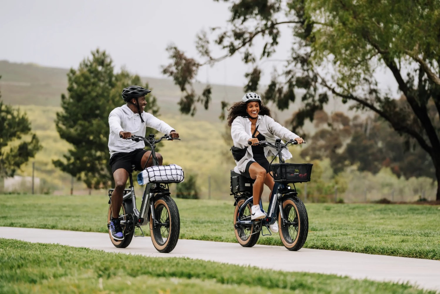 two people riding a bike down a paved trail with trees in the background